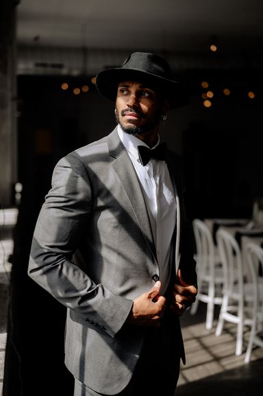 Dunkelhäutiger Mann mit Hut im Anzug schaut in der Location stehend aus dem Fenster