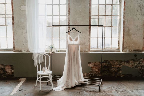 Weißes Kleid hängt an Gaderobenständer. Links daneben ein weißer Stuhl mit Schuhen.